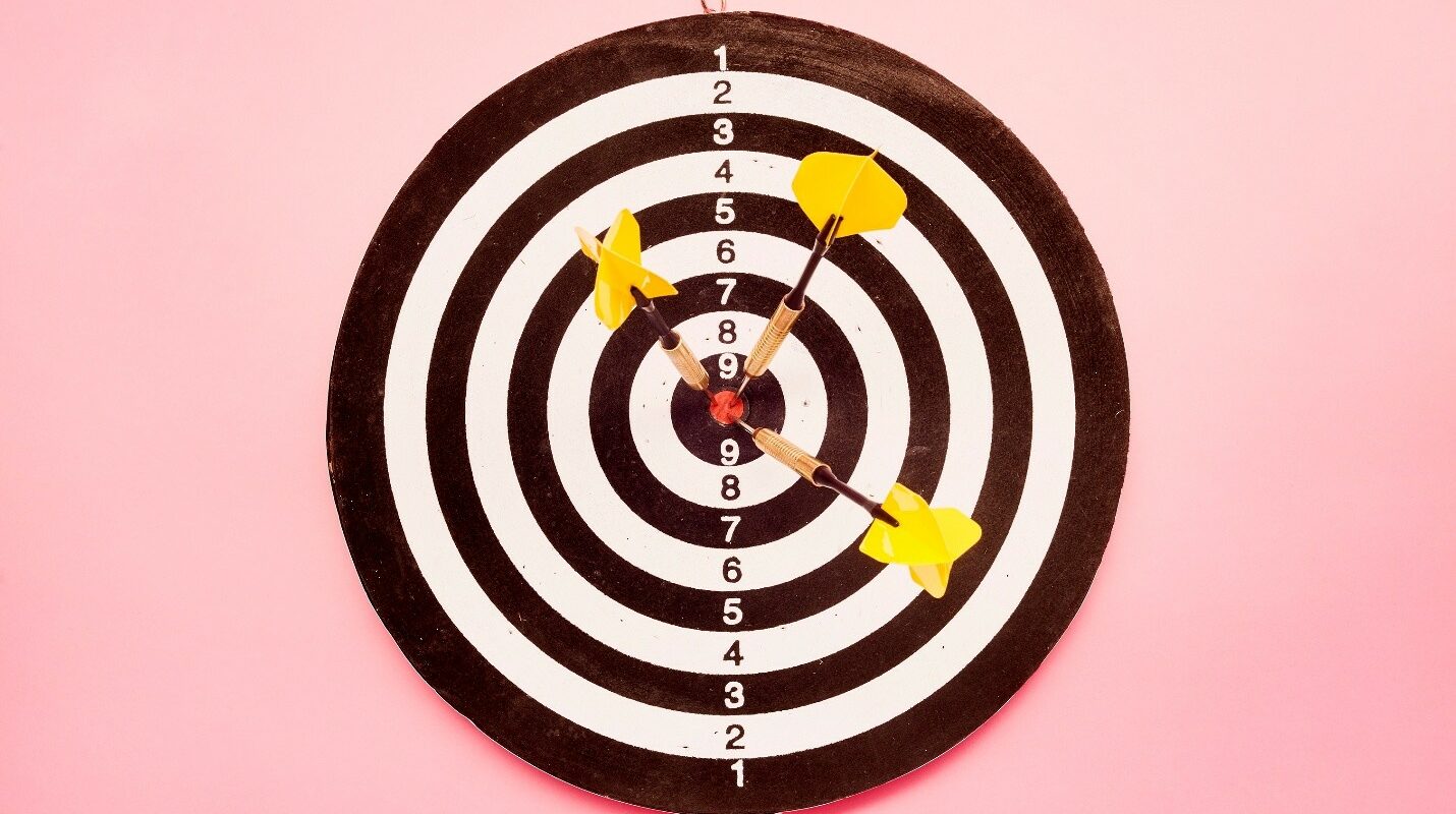 Dart board with three darts in the center point.